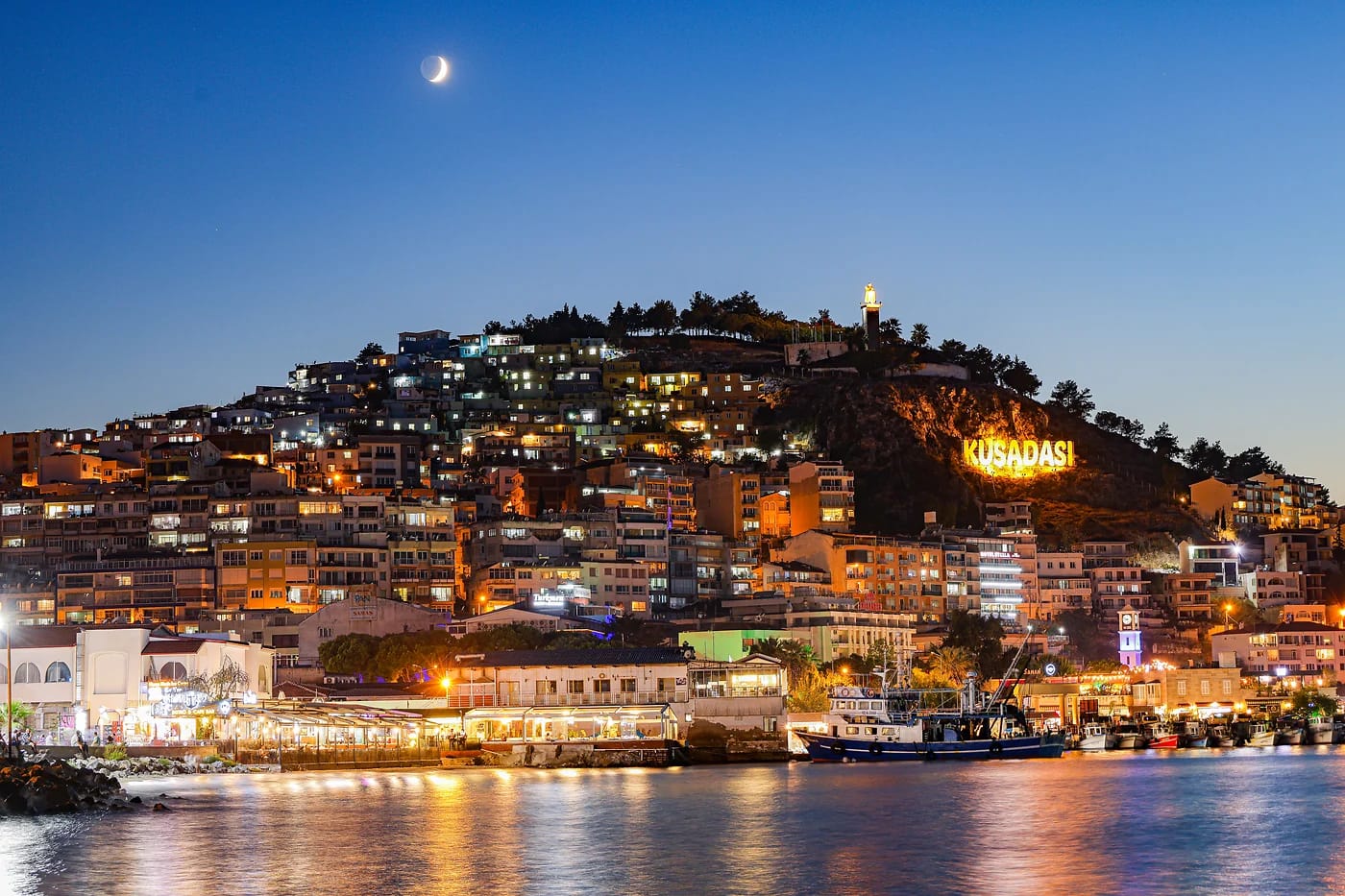 Kusadasi valaistuna yöllä ja kuunsirppi taivaalla