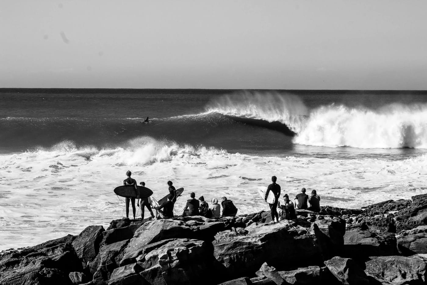 Surffaajat katsovat murtuvaa aaltoa kalliolta